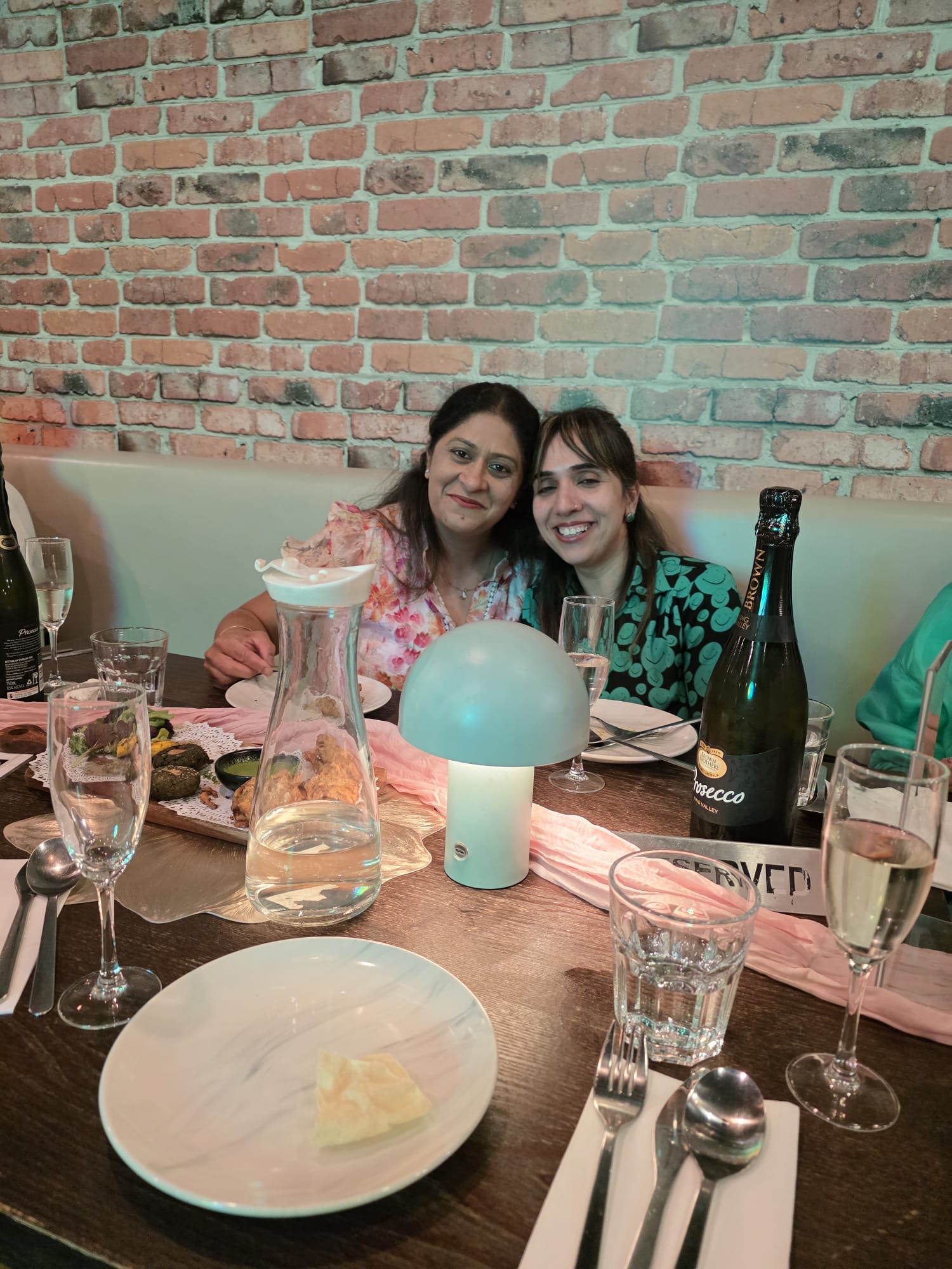Two friends smiling at a celebration table inside Aura Indian Cuisine
